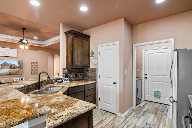 kitchen featuring a sink, light stone counters, freestanding refrigerator, arched walkways, and a raised ceiling