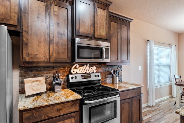 kitchen featuring tasteful backsplash, light wood finished floors, dark brown cabinets, light stone countertops, and appliances with stainless steel finishes