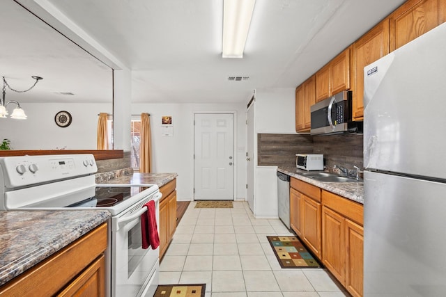 kitchen with light tile patterned flooring, brown cabinets, stainless steel appliances, and a sink