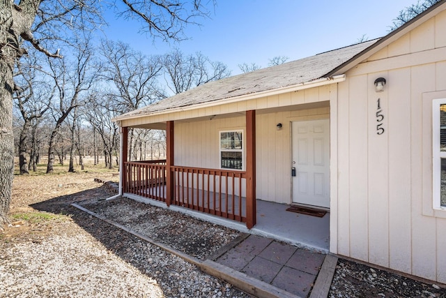 doorway to property with covered porch and a shingled roof