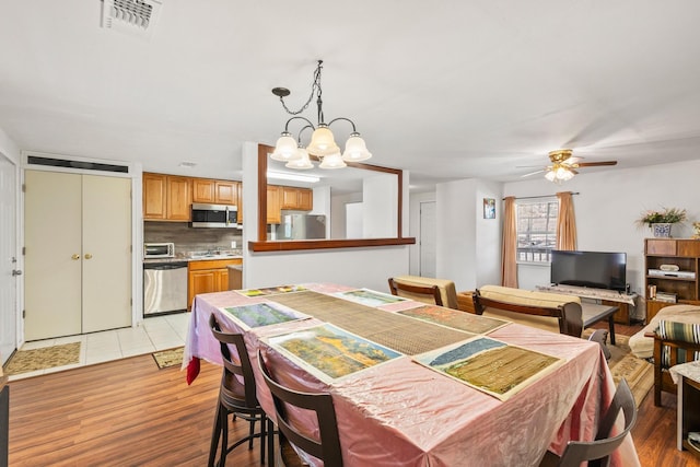 dining space featuring a toaster, ceiling fan with notable chandelier, light wood-type flooring, and visible vents