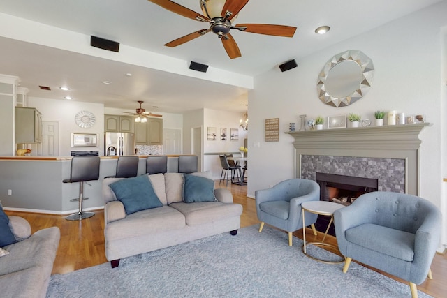 living room featuring baseboards, recessed lighting, a fireplace, ceiling fan with notable chandelier, and light wood-type flooring