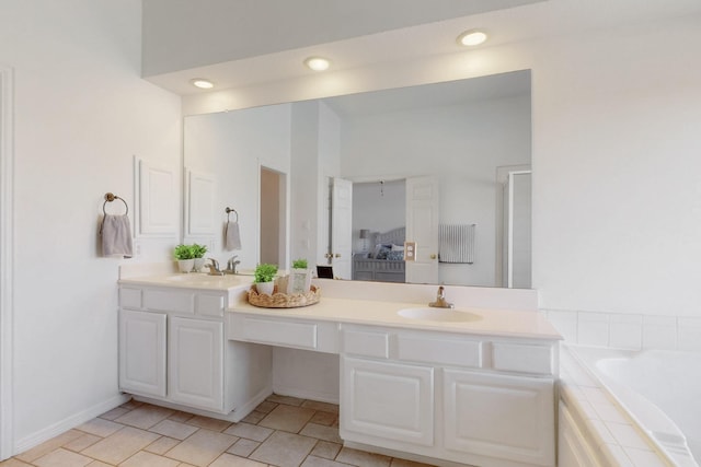 bathroom with double vanity, recessed lighting, a relaxing tiled tub, and a sink