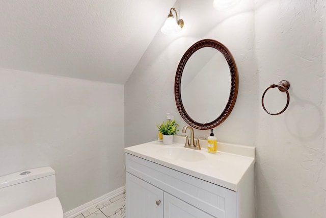 half bath featuring toilet, marble finish floor, baseboards, vanity, and vaulted ceiling