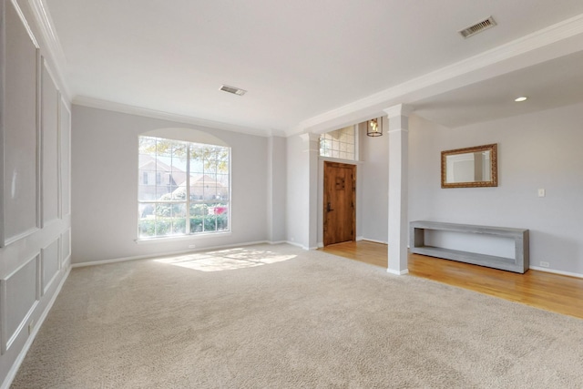 carpeted spare room featuring visible vents, baseboards, crown molding, and decorative columns