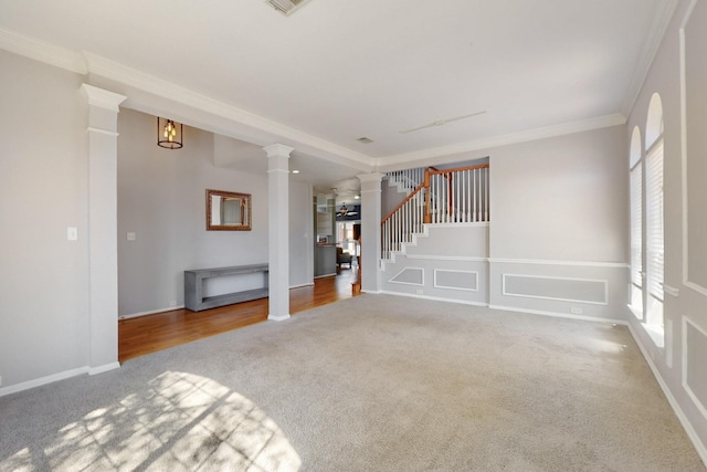 unfurnished living room with ornamental molding, carpet flooring, a decorative wall, stairs, and ornate columns