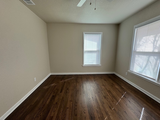 empty room with visible vents, a textured ceiling, dark wood finished floors, baseboards, and ceiling fan