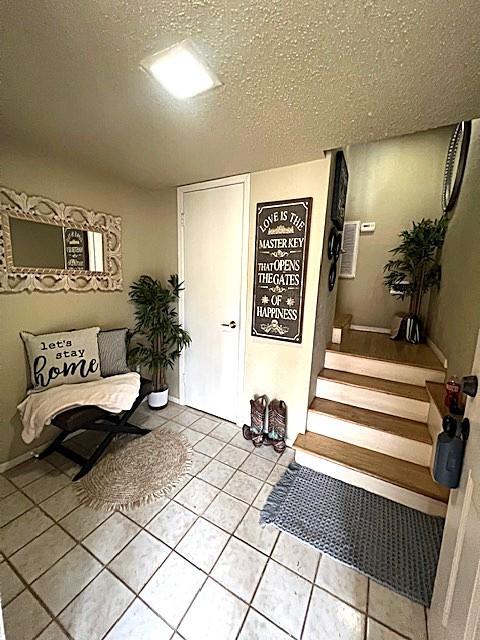 interior space featuring stairs, light tile patterned floors, and a textured ceiling