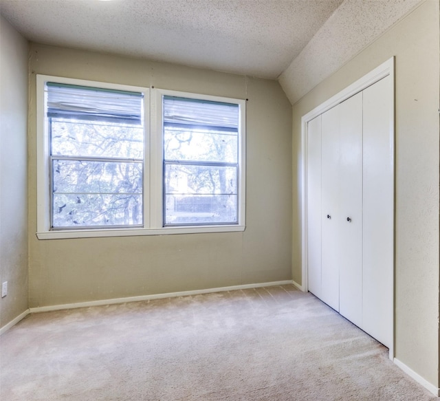 unfurnished bedroom featuring a closet, light carpet, a textured ceiling, and baseboards