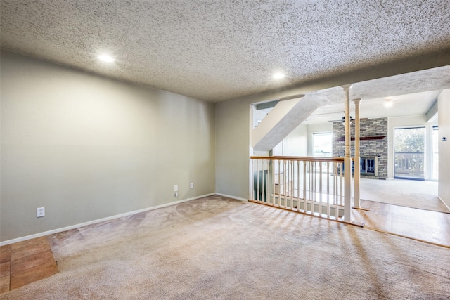 unfurnished room with a brick fireplace, a textured ceiling, carpet, and baseboards