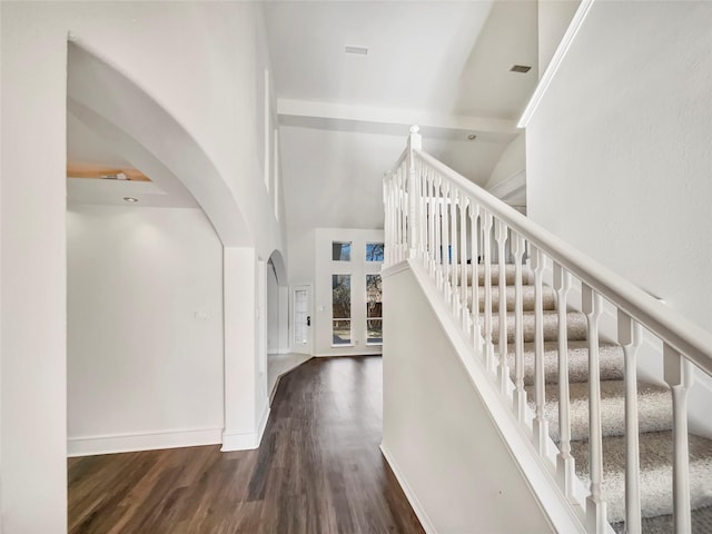 staircase featuring wood finished floors, baseboards, a towering ceiling, and arched walkways