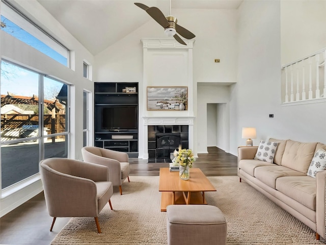 living area featuring a ceiling fan, a tiled fireplace, wood finished floors, and high vaulted ceiling