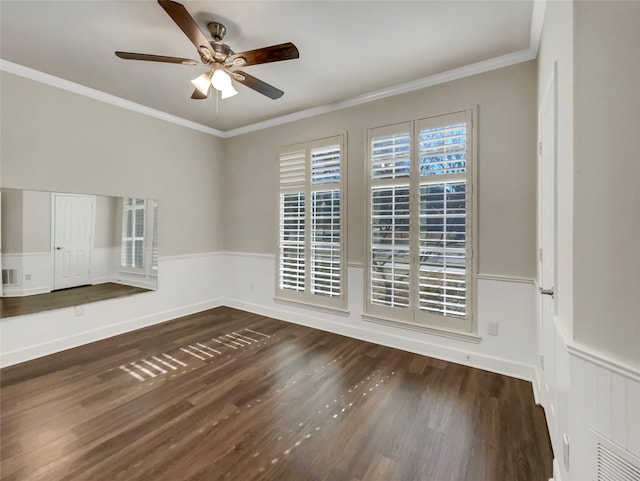 spare room featuring a ceiling fan, dark wood-style floors, a wainscoted wall, baseboards, and crown molding