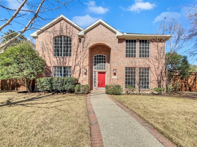 traditional-style home with brick siding, a front yard, and fence