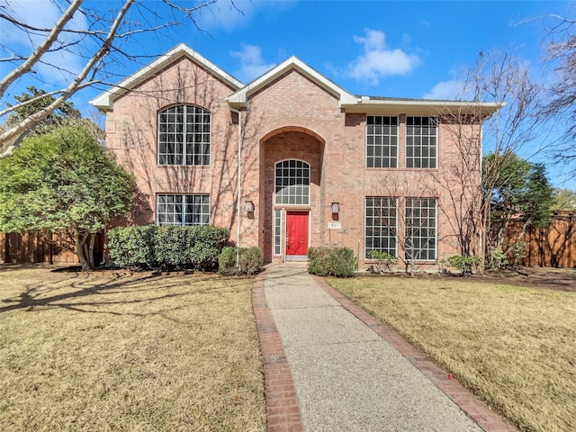 traditional-style home with a front lawn, fence, and brick siding