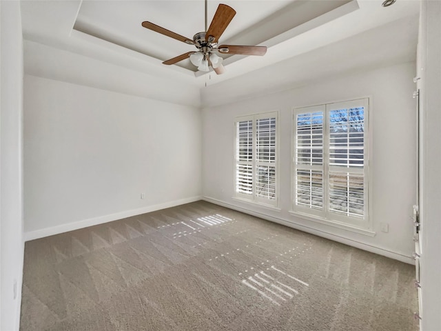 empty room with a tray ceiling, baseboards, and carpet