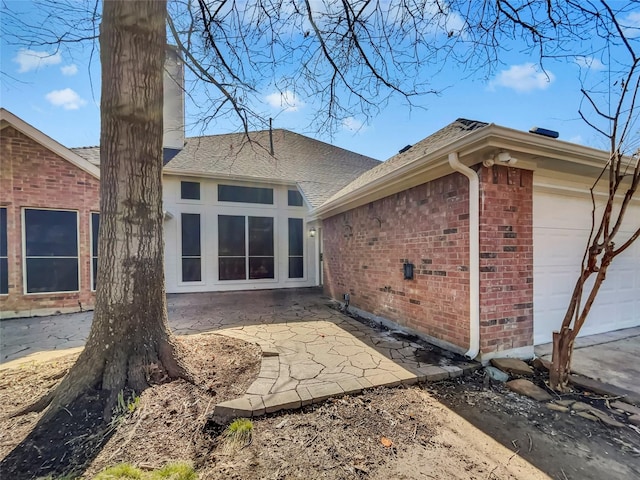 back of property with a garage, brick siding, and a patio area