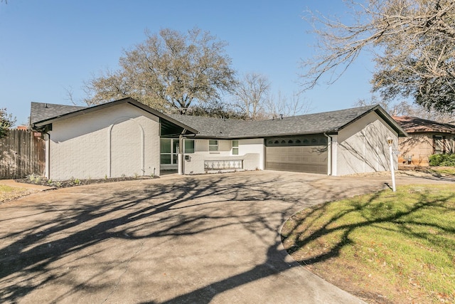 mid-century inspired home with aphalt driveway, fence, a garage, brick siding, and roof with shingles