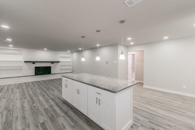 kitchen featuring light wood-style floors, stone counters, white cabinetry, visible vents, and a kitchen island