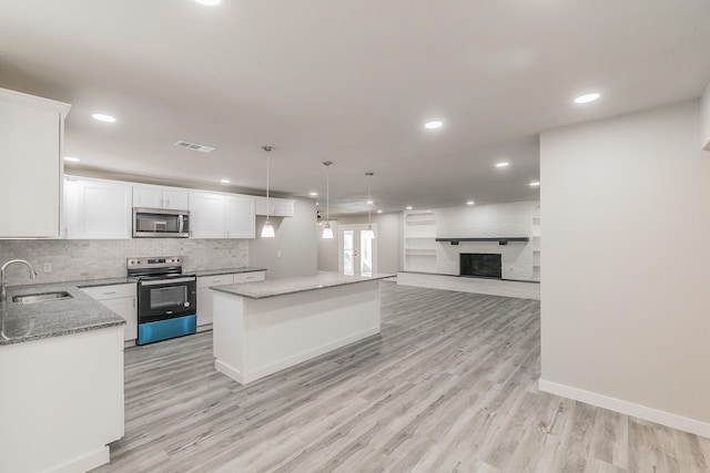 kitchen with range with electric stovetop, light stone counters, visible vents, a sink, and stainless steel microwave