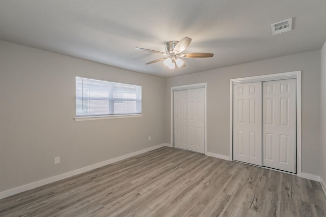 unfurnished bedroom featuring multiple closets, wood finished floors, visible vents, a ceiling fan, and baseboards