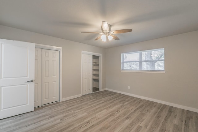 unfurnished bedroom with two closets, light wood finished floors, baseboards, and ceiling fan