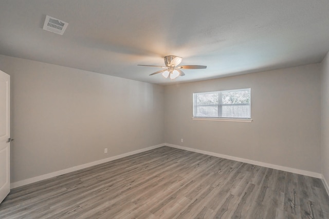 empty room with baseboards, a ceiling fan, wood finished floors, and visible vents