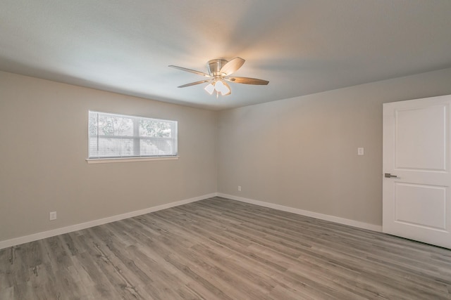 empty room with wood finished floors, a ceiling fan, and baseboards