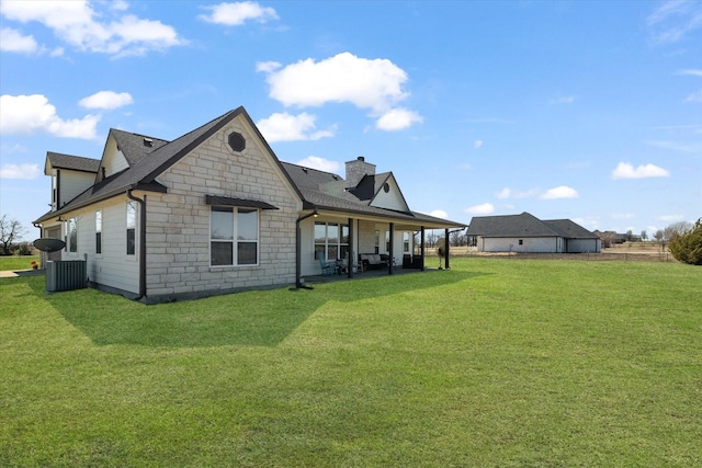 back of property featuring a patio area, stone siding, a chimney, and a yard