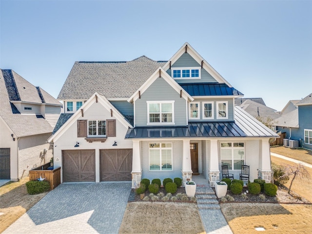 view of front facade featuring a standing seam roof, covered porch, decorative driveway, brick siding, and metal roof