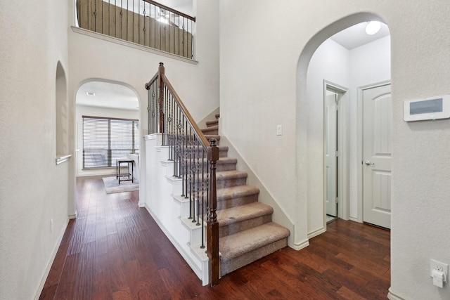 stairs featuring wood finished floors, arched walkways, and baseboards