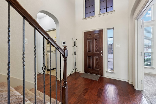 foyer entrance featuring baseboards, stairs, hardwood / wood-style flooring, arched walkways, and washer / clothes dryer