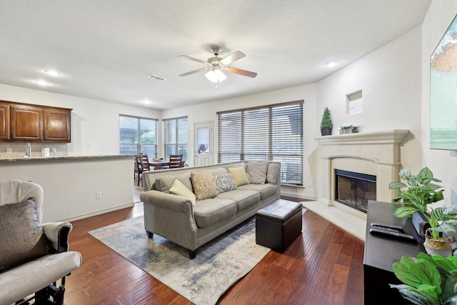 living area with visible vents, ceiling fan, a premium fireplace, dark wood-style floors, and a textured ceiling