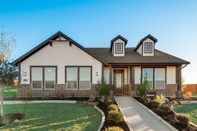 view of front of house featuring a front yard, brick siding, and a shingled roof