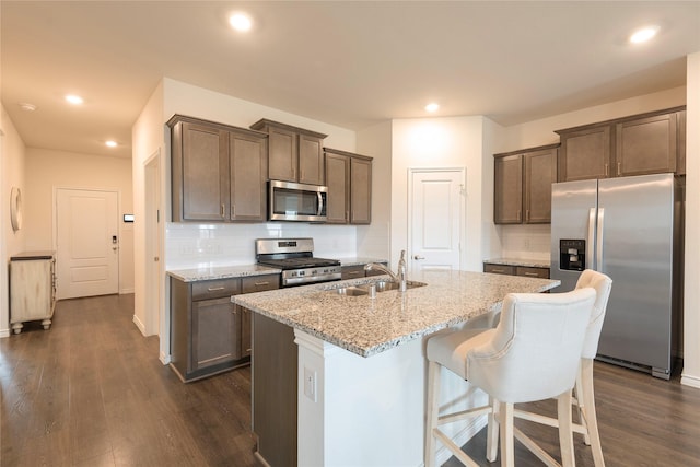 kitchen featuring dark wood-type flooring, light stone countertops, decorative backsplash, stainless steel appliances, and a sink