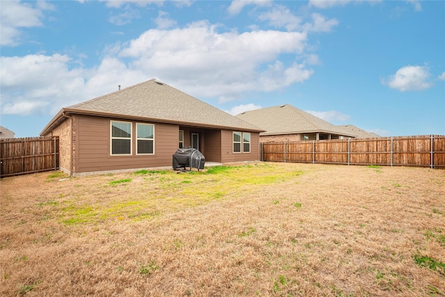 back of house featuring brick siding, a lawn, a shingled roof, and a fenced backyard