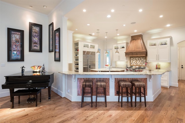 kitchen with glass insert cabinets, stainless steel built in refrigerator, a kitchen bar, custom range hood, and a peninsula