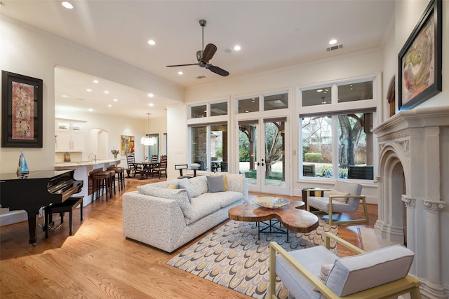 living area with recessed lighting, visible vents, light wood-style flooring, and crown molding