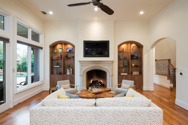 living area with built in features, arched walkways, crown molding, light wood finished floors, and baseboards