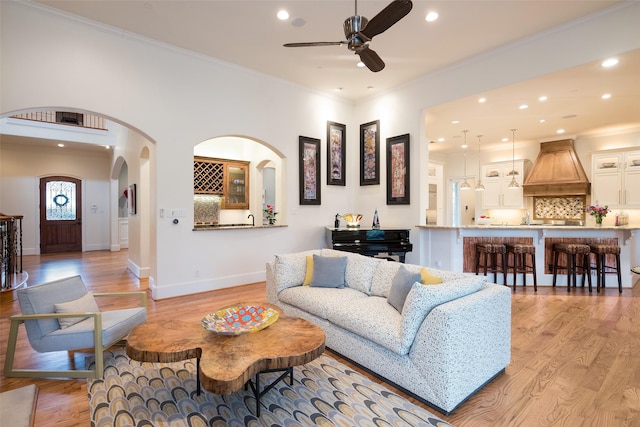 living area with arched walkways, light wood-style flooring, and crown molding