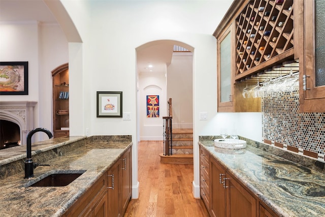 kitchen with light wood-type flooring, brown cabinets, stone counters, and a sink