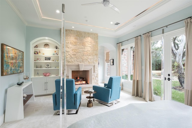 living area featuring a stone fireplace, a raised ceiling, built in features, and crown molding