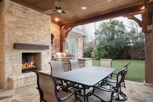 view of patio with ceiling fan, fence, an outdoor stone fireplace, outdoor dining space, and area for grilling