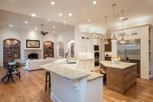 kitchen with a sink, arched walkways, a breakfast bar area, a fireplace, and built in appliances