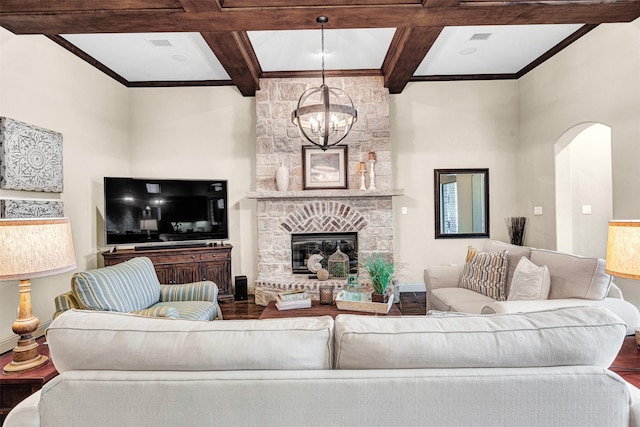 living area with wood finished floors, visible vents, coffered ceiling, a stone fireplace, and a notable chandelier