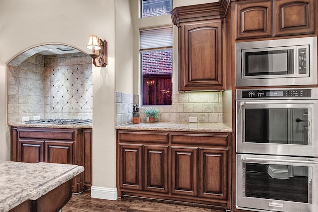 kitchen with light stone counters, tasteful backsplash, appliances with stainless steel finishes, and dark wood-style floors