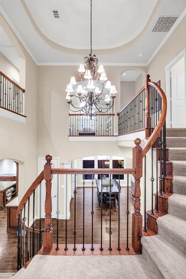 stairs with visible vents, an inviting chandelier, a tray ceiling, and wood finished floors