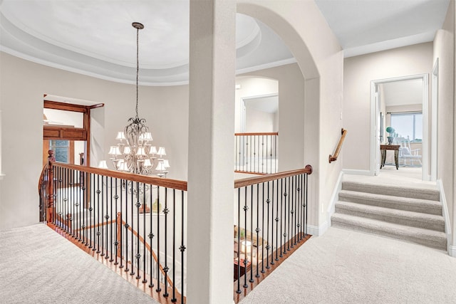 hallway with carpet, baseboards, a tray ceiling, ornamental molding, and a chandelier