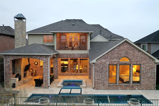 back of property with brick siding, a patio area, a shingled roof, and a balcony