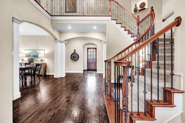 foyer featuring baseboards, ornamental molding, hardwood / wood-style floors, a towering ceiling, and arched walkways